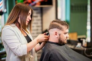 Hairdresser woman cutting hair with clipper man in barbershop photo