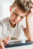 A cheerful child in a white T-shirt plays games on the phone at home. Happy boy looks at his smartphone. photo