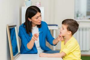 Woman speech therapist helps a child correct the violation of his speech in her office photo