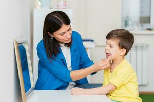 Woman speech therapist helps a child correct the violation of his speech in her office photo