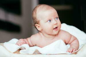 contento bebé niña mentiras en un blanco sábana en su habitación foto