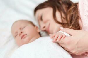 joven hermosa mujer participación pequeño mano de su dormido bebé hija en dormitorio foto