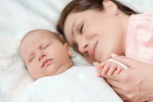 Young beautiful woman holding small hand of her sleeping baby daughter in bedroom photo