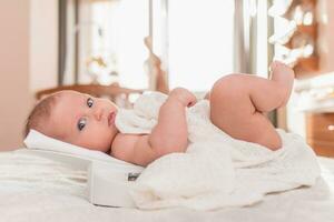 A beautiful newborn girl is weighed on an electronic scale in the bedroom photo