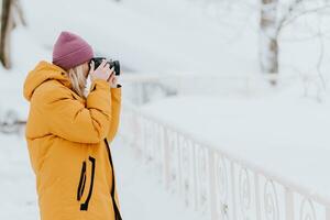 Beautiful girl in a yellow jacket photographer takes pictures of snow in a winter park photo