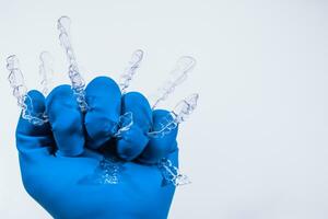 Invisible dental braces are held by a hand in a blue glove on a white background. Plastic braces dentistry retainers to straighten teeth. photo