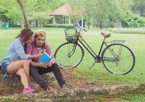 A man wear earphone for woman listen to music .They are in love in public park Thailand.lifestyle and relax time. photo