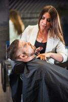 Beautiful hairdresser woman cuts man's beard at barbershop photo