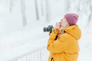 hermosa niña en un amarillo chaqueta fotógrafo toma imágenes de nieve en un invierno parque foto