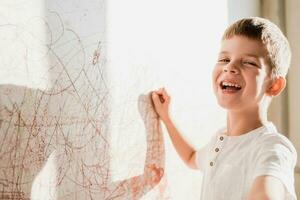 riendo niño sorteos en el pared con tiza en su habitación. el chico es comprometido en creatividad a hogar foto