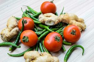 Fresco jengibre, tomate y verde chile pimienta en llanura de madera mesa, verde esencial vegetales para todas esencial alimentos, ver de sin pelar vegetales con llanura antecedentes foto