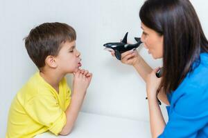 Cute woman speech therapist teaches child to pronounce words sounds and letters correctly in office photo