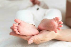 madre abrazos piernas de recién nacido bebé con manos foto