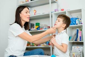 A woman speech therapist teaches a child to blow correctly on colored feathers. photo