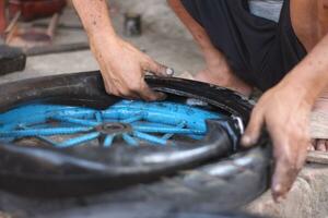 An Indonesian service worker is changing the tire of a bicycle cart manually photo