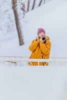 Beautiful girl in a yellow jacket photographer takes pictures of snow in a winter park photo