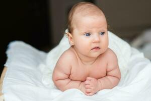 retrato de un hermosa bebé niña mentiras en un blanco sábana en su habitación foto