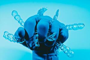 Hand in glove holds invisible dental braces on blue background. Plastic braces dentistry retainers to straighten teeth. photo