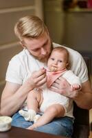 Father feeding his daughter fruit puree in the kitchen photo