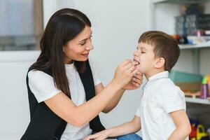 A little preschool boy is engaged in a speech therapist office and corrects his speech photo