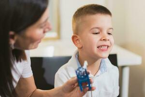 Woman speech therapist helps a child correct the violation of his speech in her office photo