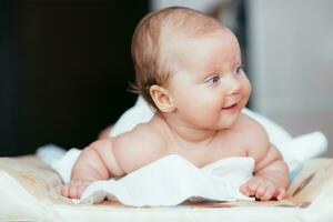 Portrait of a beautiful baby girl lies on a white sheet in her room photo