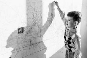 The child draws on the wall with a crayon. The boy is engaged in creativity at home. Black and white photo
