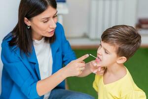 Woman speech therapist corrects speech defects in a boy in her office photo