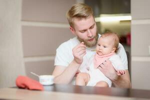 Father feeding his daughter fruit puree in the kitchen photo