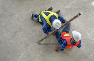 accident in site work,a piece of iron fell from height hit on a worker's legs on floor while working at a new building, a colleague rescued him from  accident.concept risk management, safety at work photo