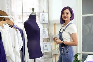 portrait young cool asian female clothing designer with purple color hair working with mannequin at her modern fashion studio,concept of fashion design.dressmaking,tailoring,business,industry photo