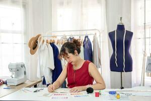 young asian female designer sketching clothing design on table,a professional dressmaker working in her modern fashion studio. concept clothing design,dressmaking,tailoring,business,industry photo