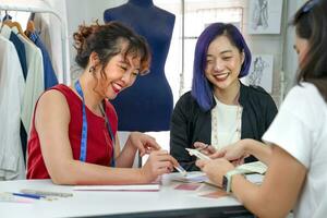 young cool female fashion designer with purple color hair and dressmaker discussing clothing design to woman customer with fashion sketch and color sample,concept of business,industry,design,tailoring photo