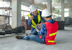 a worker wear safety gear was injured sitting on floor at site, a colleague rescued him from accident,using walkie-talkie to call first aid team.concept of risk management,accident in site work photo