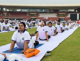 New Delhi, India, June 21, 2023 - Group Yoga exercise session for people at Yamuna Sports Complex in Delhi on International Yoga Day, Big group of adults attending yoga class in cricket stadium photo