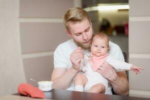 Father feeding his baby fruit puree in the kitchen photo