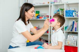 A woman speech therapist teaches a child to blow correctly on colored feathers. photo