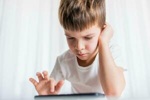 A cheerful child in a white T-shirt plays games on the phone at home. Happy boy looks at his smartphone. photo