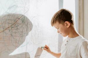 A cheerful boy with a pencil stands near the wall that he painted. A child is engaged in creativity at home. photo