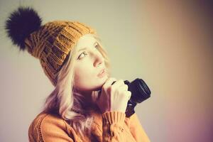 Beautiful girl photographer in a knitted hat posing with a camera in her hands in a photo studio