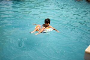 Happy Indian boy swimming in a pool, Kid wearing swimming costume along with air tube during hot summer vacations, Children boy in big swimming pool. photo