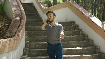 enano joven hombre hablando en el teléfono mientras caminando al aire libre. video