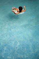 Happy Indian boy swimming in a pool, Kid wearing swimming costume along with air tube during hot summer vacations, Children boy in big swimming pool. photo