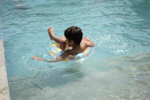 contento indio chico nadando en un piscina, niño vistiendo nadando disfraz a lo largo con aire tubo durante caliente verano vacaciones, niños chico en grande nadando piscina. foto