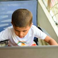 pequeño chico sentado a mesa utilizando ordenador portátil para en línea clase en grado 1, niño estudiando en ordenador portátil desde hogar para distancia aprendizaje en línea educación, colegio chico niños estilo de vida concepto foto