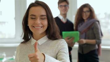 Smiling girl gestures good quality in front of man and woman with tablet video