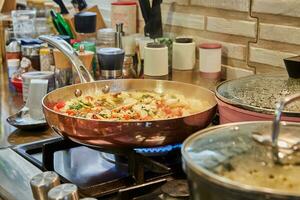 Pieces of chicken breast with tomatoes are fried in frying pan on gas stove photo