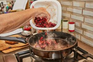 Chef fries fresh cherries in caramel syrup in frying pan on gas stove photo