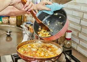 Chef puts fried onions into pieces of chicken breast with tomatoes, fried in pan on gas stove photo