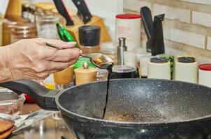 The chef pours teriyaki sauce into a frying pan on a gas stove photo